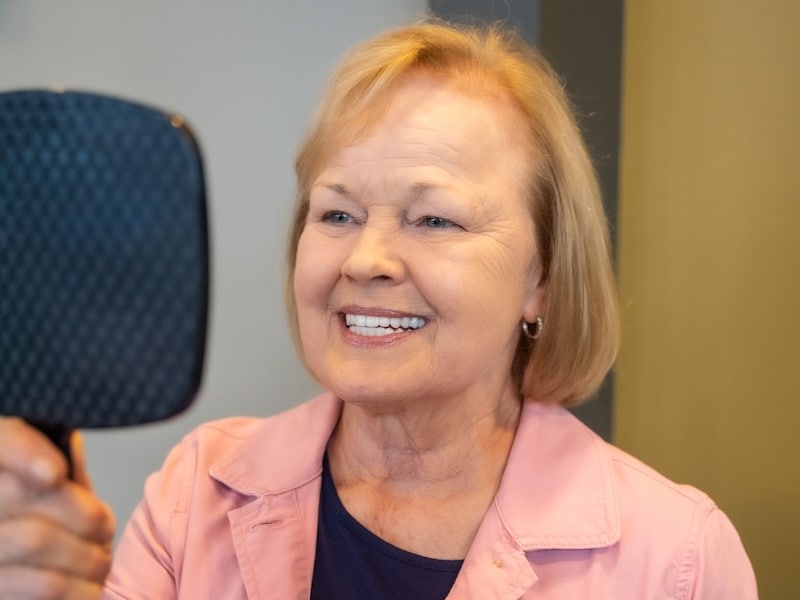 Same Day Smiles dental implant patient smiling at reflection in mirror.